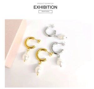 Detailed view of C-shaped 18K gold and silver earrings with Baroque pearls on white surface
