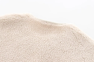 Close-up of soft beige teddy velvet fabric texture on a stylish woman's warm jacket
