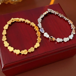 Detail of gold and silver heart-shaped chain bracelets with toggle clasp on wooden box