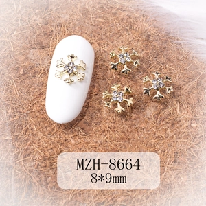 Macro detail of 8x9mm gold snowflake nail charms with white rhinestones on a nail model