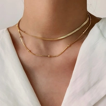 Detailed view of gold double-layer necklace with flat snake chain and bead chain on neck