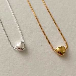 Close-up of gold and silver heart necklaces with thin square links on a clean gray background