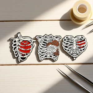 Three-piece gothic enamel skull and anatomy heart brooch pins set on wood surface