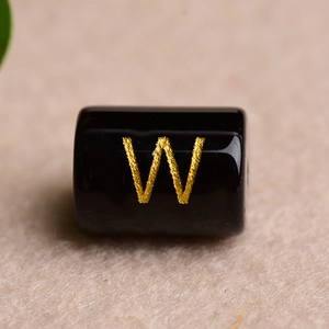 Macro shot of a black cylindrical bead featuring a gold-engraved letter W for DIY jewelry