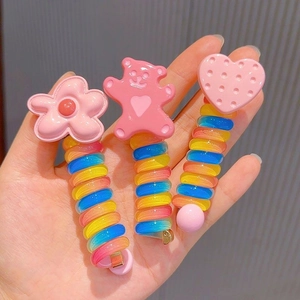 Close-up of three rainbow spiral hair ties with pink flower, bear and heart charms