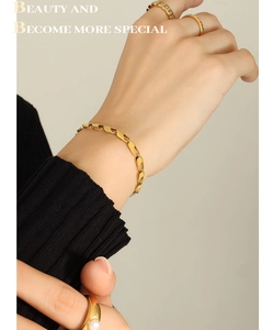 Close-up of a gold link chain bracelet with layered pearl and diamond rings on a model