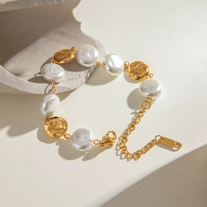 Detail of gold hammered metal and white baroque pearl bracelet on minimalist stone backdrop