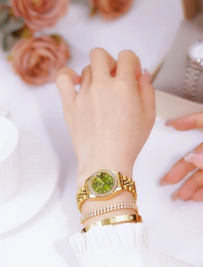 Close-up of women's gold watch with green dial and diamond markers worn by a model
