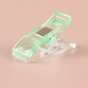 Detail view of a green plastic sewing clip with a strong metal spring on pink background