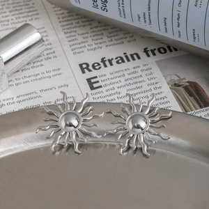 Detailed close-up of polished silver sun stud earrings on a textured metal tray