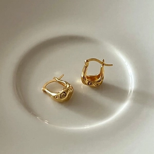 Detailed macro shot of irregular golden lava texture earrings on a white ceramic plate