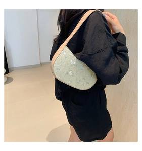 Detail of light green straw woven bag with white flower embroidery on model's shoulder