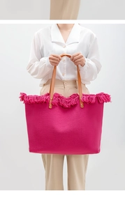 Detail of fuchsia woven tote bag featuring fringe trim and brown leather handles