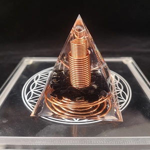 Macro detail of resin orgone pyramid with copper coil and black crystal on glass base