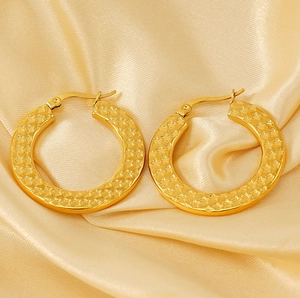 Detail of gold stainless steel hoop earrings with star embossed texture on silk background