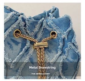 Detail showing the golden metal drawstring on frayed denim fabric of a stylish bag