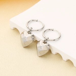 Macro detail of geometric faceted heart pendant earrings with polished metallic silver finish