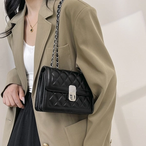 Detail view of black quilted crossbody bag with silver chain strap on model's shoulder