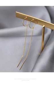 Macro shot of gold long chain tassel earrings displayed on a luxury silk fabric background