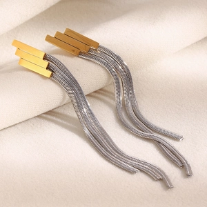 Detail of 18K gold geometric studs with silver snake chain tassels on soft fabric