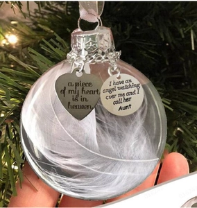 Close-up of commemorative Christmas ornament featuring white feathers and engraved metal charms