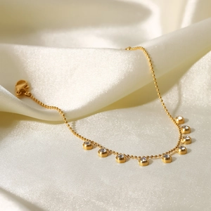 Detail of gold beaded chain necklace with zircon charms on white silk fabric