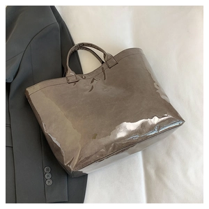 Close-up of a large glossy brown faux leather tote bag next to a grey suit jacket