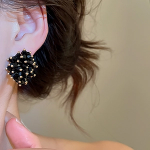 Close-up of irregular black crystal stud earrings with gold accents on model ear
