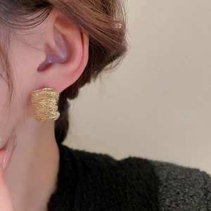 Detailed view of wide golden earrings featuring unique irregular layered texture and metallic gloss