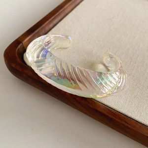 Detailed view of iridescent geometric open bangle with spiral texture on display tray