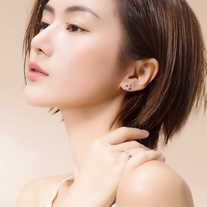 Close-up of elegant flower stud earrings and slender silver ring on a female model
