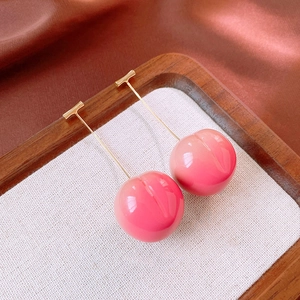 Macro detail of sweet pink resin peach drop earrings on a warm wooden display tray