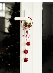 Close-up of a Christmas door hanger with red metal bells and green pine needles on a handle