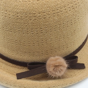Detail of light khaki knit hat featuring a brown suede bow and a soft pink pom-pom decoration