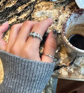 Close-up of stacked retro oval beaded silver ring and minimalist wavy band on model's hand