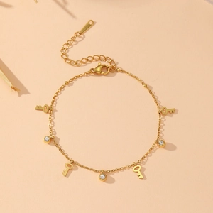 Détail du bracelet en acier inoxydable doré avec breloques clés et zircons étincelants