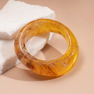 Close-up of amber resin bangle with tortoiseshell pattern on white textured stones