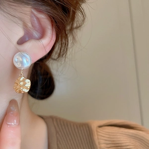 Close-up of elegant gold wrinkled metal earrings with white pearls on a female model