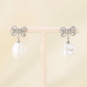 Detail of silver bow earrings with pavé stones and baroque pearls on a pink stand