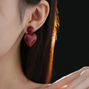 Close-up of a model wearing minimalist deep red heart pendant earrings with sleek finish
