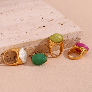Detail shot of four gold-plated rings with colorful irregular acrylic stones on stone texture