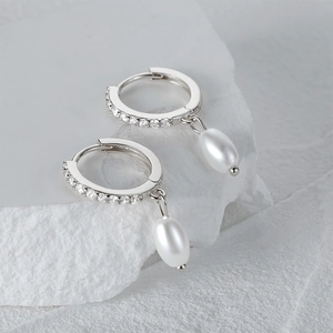 Close-up of elegant silver hoop earrings with zircon and white teardrop pearls on stone