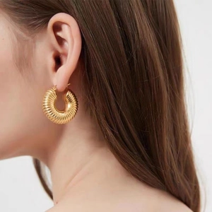 Close-up of golden chunky hoop earrings with textured spiral design worn by a model