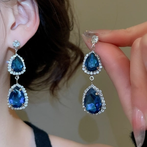 Close-up of elegant silver drop earrings featuring radiant blue crystals and halo diamonds