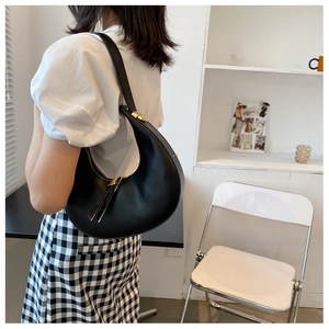 Minimalist black crescent hobo shoulder bag with gold metal hardware worn by a model