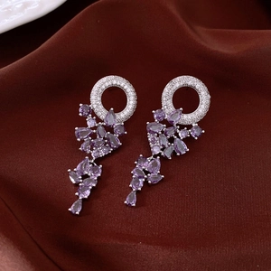Detail of silver drop earrings with purple zirconia crystals and tassels on silk background
