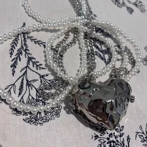 Macro detail of silver liquid metal heart pendant and pearl chain on floral fabric