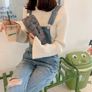 Gray corduroy pencil case with bear embroidery shown in a minimalist cafe setting