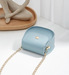 Macro shot of light blue mini saddle bag with gold metal buckle and fine chain strap