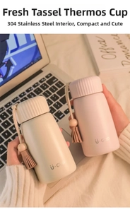 Mini stainless steel vacuum flask with tassel charm held against lifestyle background